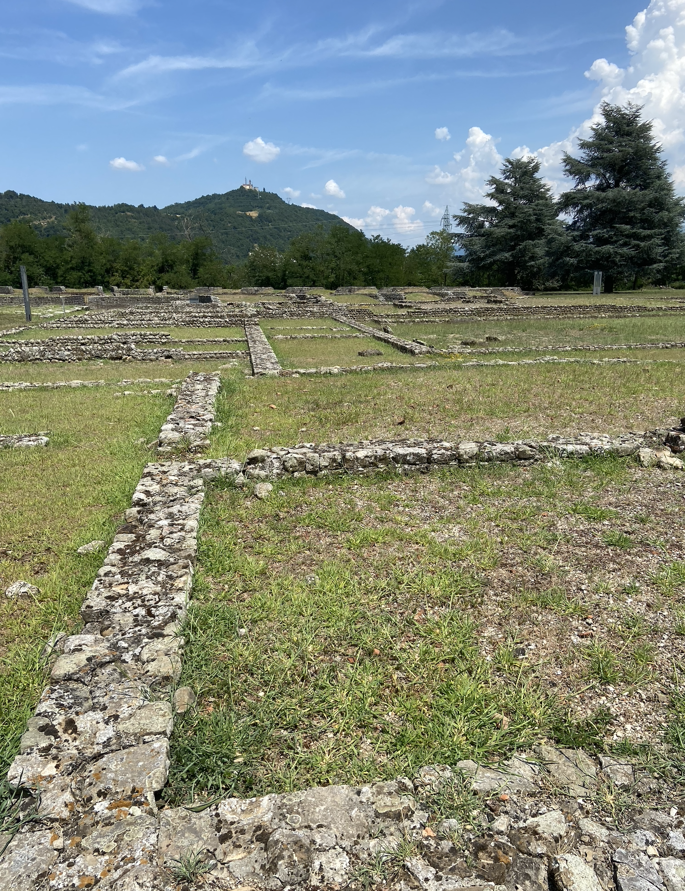 stone foundations of now missing ancient walls in a grassy field with a monastery on a hill in the distance